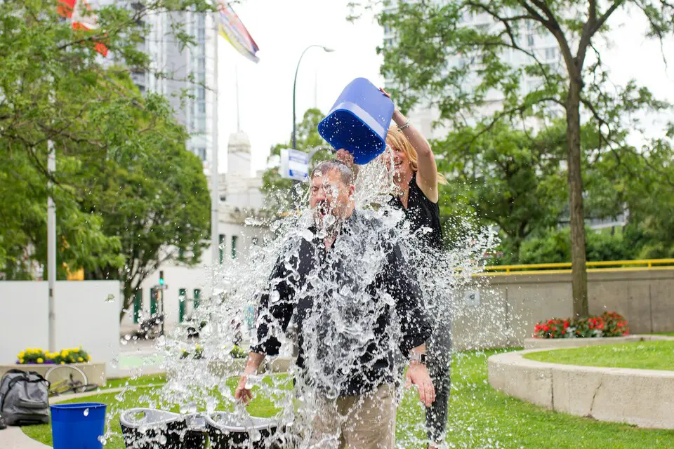 Photo shows a white male wearing a black shirt having ice thrown on him from a bucket by someone else as part of team building experience.